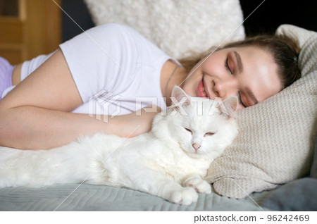 Cute girl sleeping on a bed next to a white cat Cute girl sleeping on a bed next to a white cat 96242469