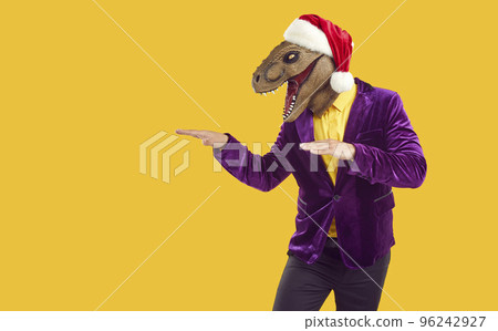 Man in funny dinosaur mask and Xmas hat advertises holiday sale on yellow copy space background 96242927
