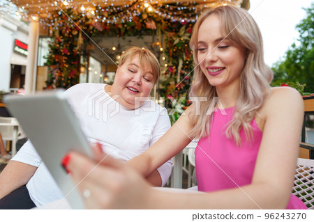 Mother with disability in wheelchair and her daughter using digital tablet while sitting at the table in cafe Mother with disability in wheelchair and her daughter using digital tablet while sitting at the table in cafe 96243270