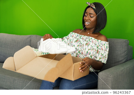 African young woman sit on couch at home unpack cardboard box with online purchase African young woman sit on couch at home unpack cardboard box with online purchase 96243367