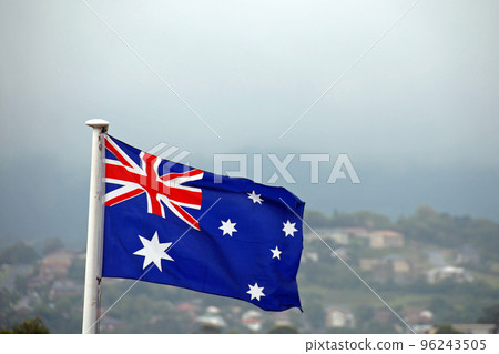 Australian flag set against a background of houses on a hill and sky. The Australian flag features six stars and the British union jack. 96243505
