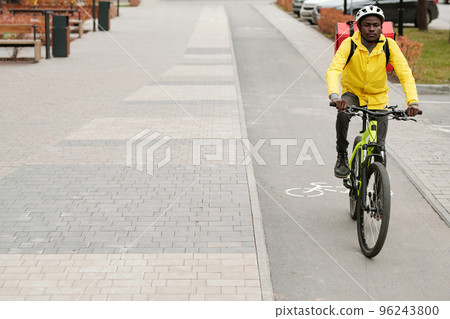 Young African American male courier with backpack riding bicycle 96243800