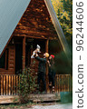 A happy family at a wooden house in the forest. A happy young couple with a child at the cottage. A young family. A young family is vacationing outside the city. Copy space 96244606