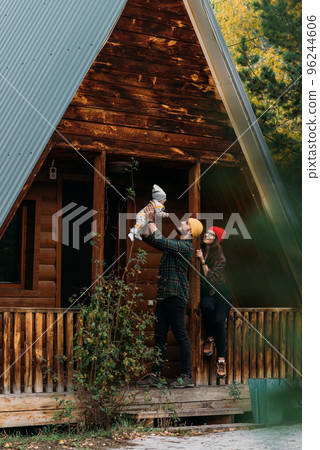 A happy family at a wooden house in the forest. A happy young couple with a child at the cottage. A young family. A young family is vacationing outside the city. Copy space 96244606