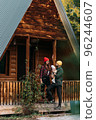 A happy family at a wooden house in the forest. A happy young couple with a child at the cottage. A young family. A young family is vacationing outside the city. Copy space 96244607