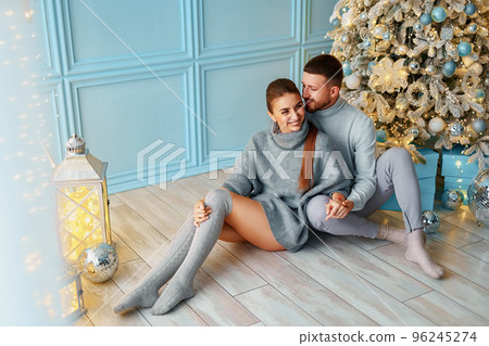 happy couple sitting and hugging near Christmas tree at home. hearth, home clothes and sweaters 96245274