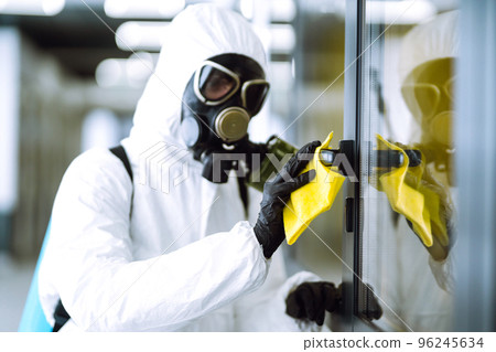 Man in protective hazmat suit washes door handles in office to preventing the spread of coronavirus. 96245634