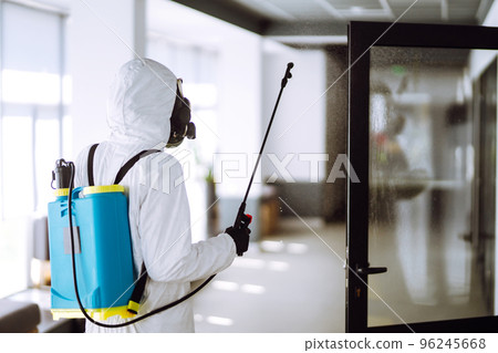 Disinfecting of office to prevent COVID-19, Man in protective hazmat suit with spray chemicals. Disinfecting of office to prevent COVID-19, Man in protective hazmat suit with spray chemicals. 96245668
