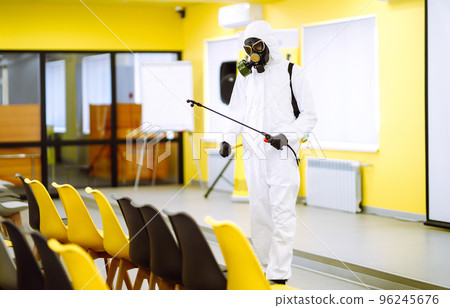 Man wearing protective suit disinfecting assembly hall with spray. Disinfecting of office. COVID-19. 96245676
