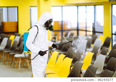 Man wearing protective suit disinfecting assembly hall with spray. Disinfecting of office. COVID-19. 96245677
