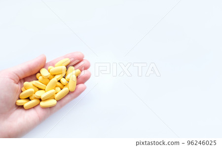 Close-up texture of yellow multivitamin tablets in female hand on white background. Healthy lifestyle concept Close-up texture of yellow multivitamin tablets in female hand on white background. Healthy lifestyle concept 96246025