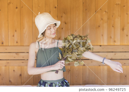 Young woman using vihta in sauna 96249725