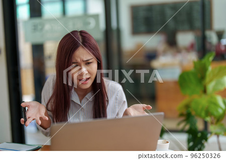 Portrait of an Asian female employee using a computer to confer with a business partner with a serious expression on solution negotiations, marketing planning and budget management. 96250326