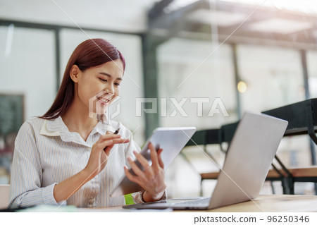 Portrait of an Asian female employee using a tablet computer to work to gather information and analyze marketing plans and investment budgets to increase company profits. Portrait of an Asian female employee using a tablet computer to work to gather information and analyze marketing plans and investment budgets to increase company profits. 96250346