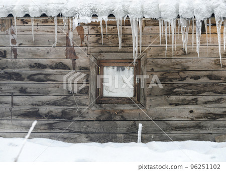 A small window and icicles on the roof an old wooden stable in winter 96251102