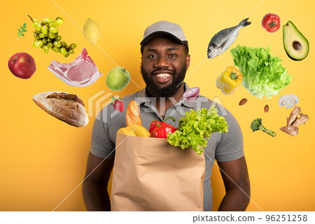 Deliveryman with happy expression ready to deliver bag with food. Yellow background. Deliveryman with happy expression ready to deliver bag with food. Yellow background. 96251258