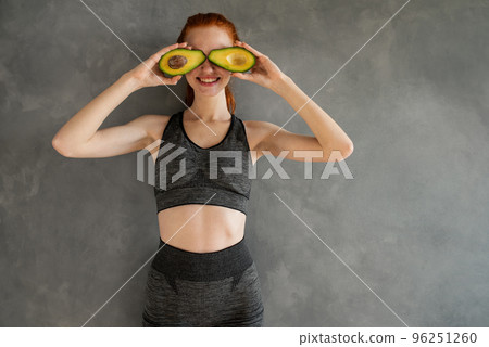 Athletic girl with gym clothes eats avocado at home. Athletic girl with gym clothes eats avocado at home. 96251260