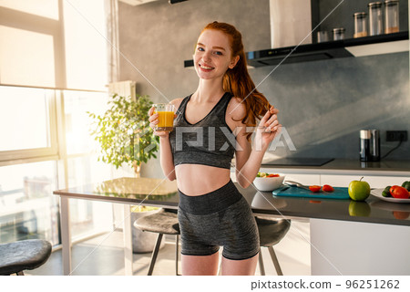 Athletic girl with gym clothes drinks a orange juice in the kitchen 96251262