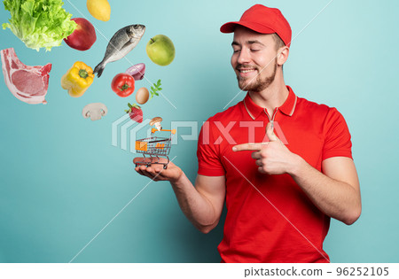 Deliveryman holds a small cart that is filled with food. Cyan background Deliveryman holds a small cart that is filled with food. Cyan background 96252105