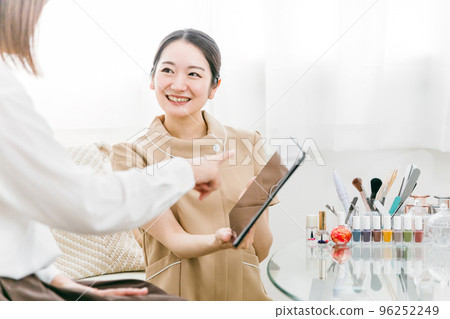 Japanese woman receiving counseling from a manicurist using a tablet at a nail salon Japanese woman receiving counseling from a manicurist using a tablet at a nail salon 96252249
