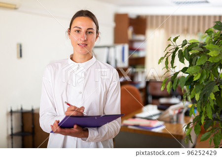 Portrait of a young female manager standing in a office and making notes 96252429