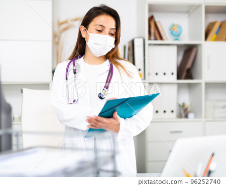 Female therapist in a medical mask fills out a patient's treatment appointment sheet on a tablet in the office Female therapist in a medical mask fills out a patient's treatment appointment sheet on a tablet in the office 96252740