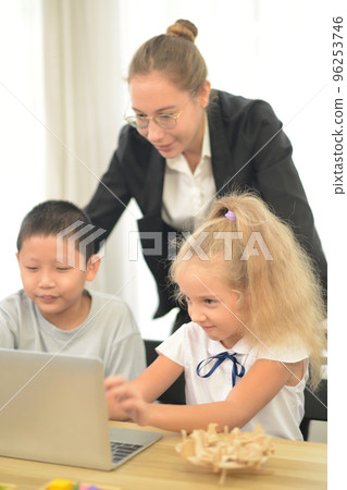Friendly teacher helping primary school in computer class. Friendly teacher helping primary school in computer class. 96253746