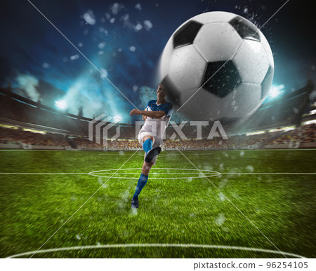 Football scene at night match with player in a white and blue uniform kicking the ball with power 96254105