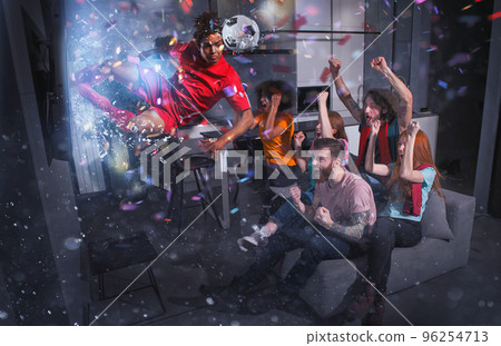 Group of friends watch a football match on television with a soccer player who exits from screen Group of friends watch a football match on television with a soccer player who exits from screen 96254713