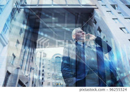 Senior businessman speaks on the mobile while walking in a modern city. Double exposure effect 96255524