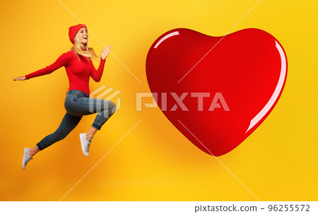 Blonde young girl jumps to reach a big heart. Concept of relationship, meeting on social network Blonde young girl jumps to reach a big heart. Concept of relationship, meeting on social network 96255572