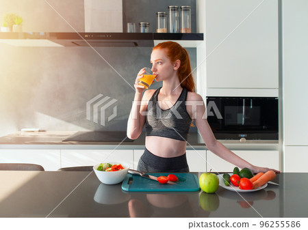 Athletic girl with gym clothes eats fruit in the kitchen 96255586