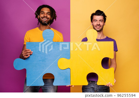 Friends with puzzles in hand over yellow background. Concept of integration, union and partnership Friends with puzzles in hand over yellow background. Concept of integration, union and partnership 96255594