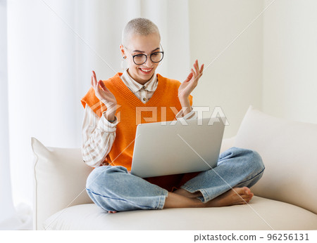 Beautiful woman freelancer with very short hair working at laptop, makes a video call and happily gestures at home 96256131