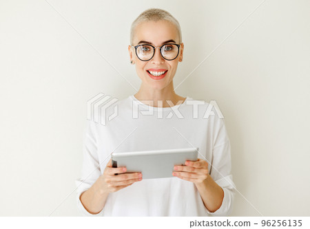 Beautiful woman freelancer with very short hair holding tablet and looking at camera on blank wall Beautiful woman freelancer with very short hair holding tablet and looking at camera on blank wall 96256135