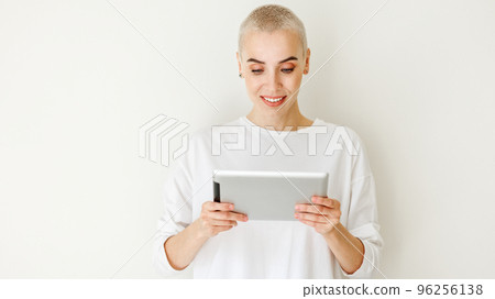 Beautiful woman freelancer with very short hair holding tablet on blank wall 96256138