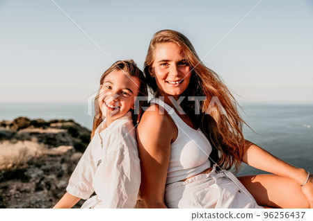 Sea family vacation together, happy mom and teenage daughter hugging and smiling together over sunset sea view. Beautiful woman with long hair relaxing with her child. Concept of happy friendly family 96256437