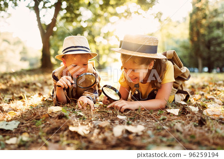 Two little kids with backpacks examining plants through magnifying glass in forest Two little kids with backpacks examining plants through magnifying glass in forest 96259194