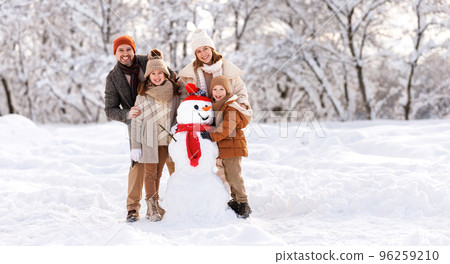 Happy children sculpting funny snowman together with parents in winter snow-covered park Happy children sculpting funny snowman together with parents in winter snow-covered park 96259210