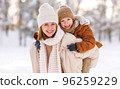 Mom giving piggyback ride to happy little son while walking outdoors in snowy winter park 96259229