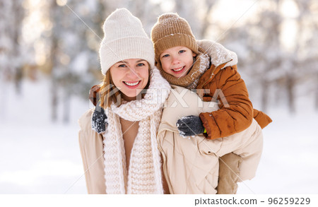Mom giving piggyback ride to happy little son while walking outdoors in snowy winter park 96259229