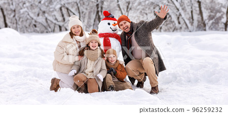 Happy family in warm clothes laughing merrily while making snowman together Happy family in warm clothes laughing merrily while making snowman together 96259232