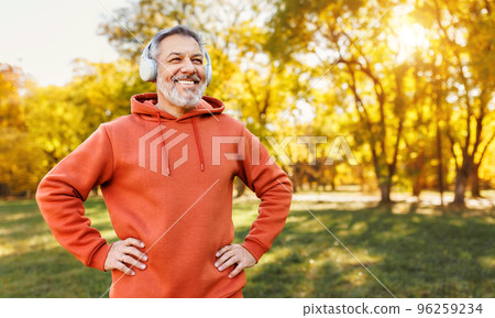 Happy positive mature man with broad in headphones smile while doing sport in city park Happy positive mature man with broad in headphones smile while doing sport in city park 96259234