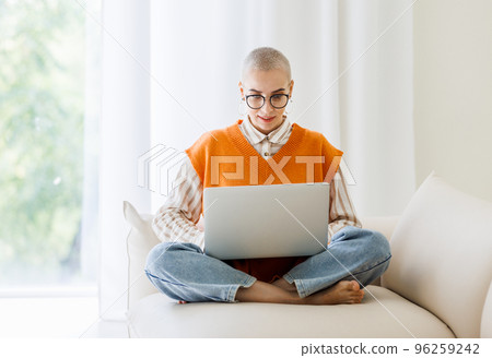 Full height of beautiful woman freelancer in glasses with very short hair working at laptop at home Full height of beautiful woman freelancer in glasses with very short hair working at laptop at home 96259242