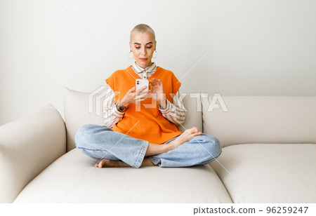 Young beautiful woman with very short hair relaxing at home with smartphone, surfing internet Young beautiful woman with very short hair relaxing at home with smartphone, surfing internet 96259247