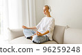 Relaxed young woman in wireless headphonesmeditating on sofa 96259248