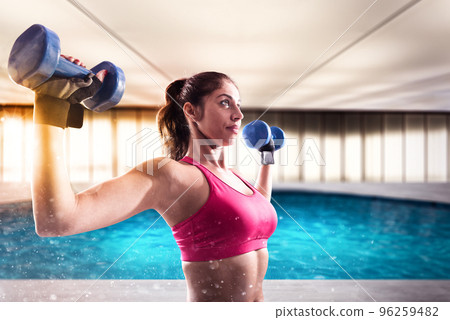 Muscular woman is training with weights dumbbells 96259482