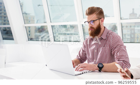 Hipster businessman at the office working with a laptop with his team Hipster businessman at the office working with a laptop with his team 96259555