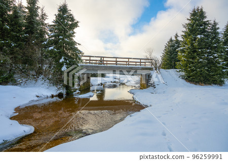 Bridge over calm mountain creek in wintertime. Cold and snowy day in Jizera Mountains. Jizerka, Czech Republic Bridge over calm mountain creek in wintertime. Cold and snowy day in Jizera Mountains. Jizerka, Czech Republic 96259991
