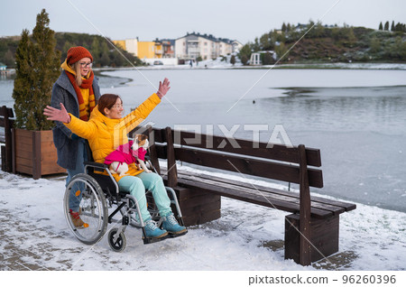 Caucasian woman driving her friend in a wheelchair along the lake in winter. 96260396